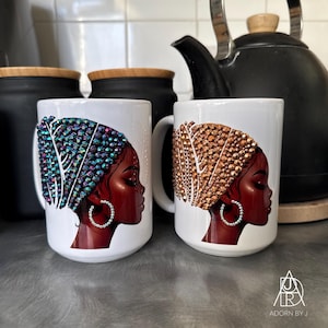 Peut inclure: Deux mugs en céramique blanche avec un portrait de profil d'une femme portant un foulard orné de bijoux. L'un des mugs présente un foulard bleu et violet, l'autre un foulard doré. Les deux mugs ont une anse blanche et une boucle d'oreille argentée.