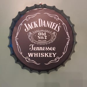 May include: A black metal bottle cap with a white Jack Daniel's logo. The logo says "Jack Daniel's" with "Old No. 7 Brand" underneath and "Tennessee WHISKEY" below that.