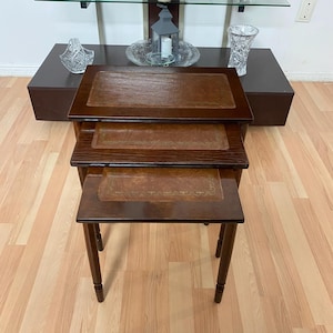 May include: A set of three antique nesting tables. The tables are made of dark wood with a rectangular top and a leather insert. The legs are turned and the tables vary in size. The largest table is approximately 61 cm long.