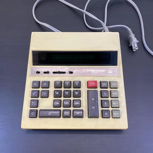 May include: A white ceramic mug with a black handle and the text "But First, Coffee" in a black, handwritten-style font. The mug is on a white surface.