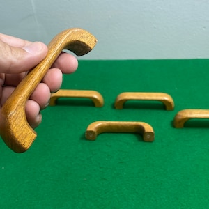 May include: Five wooden cabinet door pulls in a light brown colour. The pulls are shaped like a half-circle and have a smooth finish.