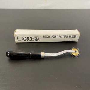 May include: A needle point pattern tracer with a black handle and a brass spiked wheel. The tool is labelled "LANCE" and "NEEDLE POINT PATTERN TRACER" on the packaging. The tool is made in Japan.