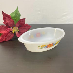 Op de afbeelding: Ovale, crèmekleurige serveerschaal met een bloemenpatroon in rood, blauw, geel en oranje. De schaal heeft een licht verhoogde rand. Een rode poinsettia bloem staat op de achtergrond.