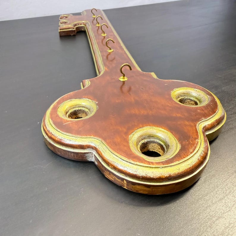 May include: A wooden key-shaped key holder for wall mounting. The key has a dark brown finish with gold-coloured trim and brass hooks for hanging keys. The key holder is approximately 30 cm long.