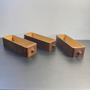 Könnte beinhalten: Drei Holzkisten mit Schubladen in dunkelbrauner Farbe. Jede Kiste hat einen kleinen runden Knopf an der Vorderseite.