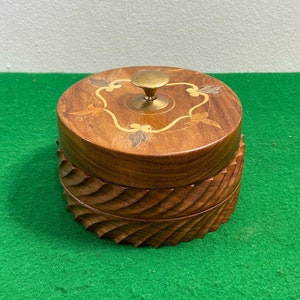 Puede incluir: Una caja de madera con una tapa tallada y un pomo de latón. La tapa está decorada con madera incrustada en un patrón floral.