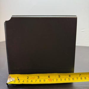 May include: A black, rectangular object with a slightly curved edge. The object is measured with a yellow tape measure, showing a length of approximately 7 inches. The object has a matte finish and appears to be made of metal or a similar material.