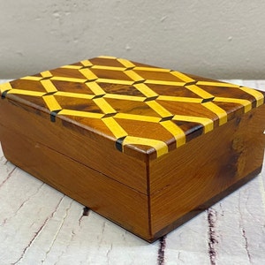 May include: A wooden box with a geometric pattern on the lid. The pattern is made of yellow and brown wood pieces. The box is made of dark brown wood.