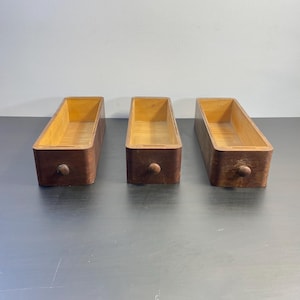 Op de afbeelding: Drie houten ladeboxen met een donkerbruine vlek en een licht houten interieur. Elke doos heeft een ronde knop aan de voorkant.