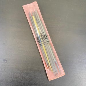 May include: A packet of Hero brand knitting needles in a pink plastic sleeve. The needles are silver and yellow, with the brand name and location printed on the packaging. Made in the USA.