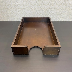 May include: A rectangular dark brown wooden desk tray with high sides and a U-shaped cutout on the front panel. The tray features visible finger joint construction on the corners and a smooth, flat interior base for organizing documents or papers.