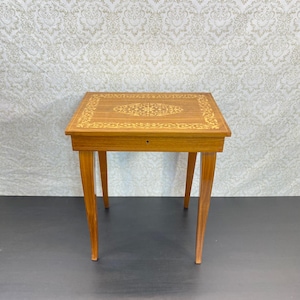 Peut inclure: Une table d'appoint rectangulaire en bois avec une finition brun clair et des motifs de marqueterie incrustés sur le plateau. La table repose sur quatre pieds fuselés et comprend un tiroir frontal unique avec une petite entrée de serrure.