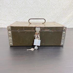 May include: A rectangular olive green metal lockbox featuring reinforced silver-toned metal corners, a top-mounted carrying handle, and a central latch mechanism secured with a silver padlock and a single metal key hanging from the shackle.