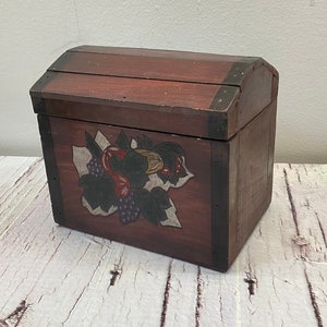 Op de afbeelding: Een kleine houten doos met een scharnierend deksel en een geschilderd ontwerp van druiven en bladeren. De doos is geschilderd in tinten bruin, rood en groen.