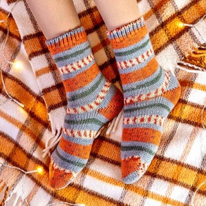 May include: A pair of hand-knitted socks featuring a multi-colored striped pattern in shades of orange, grey, and green. The socks have a ribbed cuff at the top and a textured knit construction throughout, covering the feet and ankles completely.