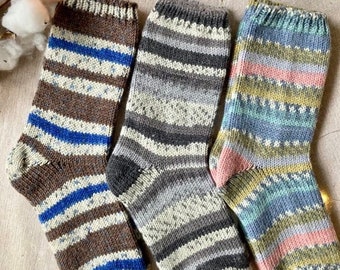 Könnte beinhalten: Drei Paar gestrickte Socken mit Streifen in Braun-, Grau- und Blautönen. Die Socken sind aus verschiedenen Garnen gefertigt und haben eine strukturierte Strickart.