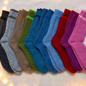 Op de afbeelding: Een verzameling van tien paar pluche sokken in verschillende kleuren, waaronder roze, paars, rood, blauw, groen, bruin en grijs. De sokken zijn in een rij gerangschikt, met de tenen naar de kijker gericht.