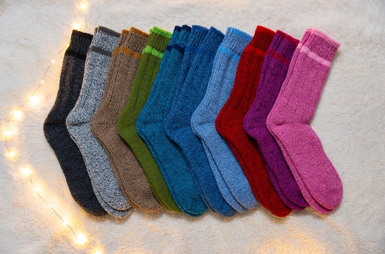 May include: A collection of ten pairs of fuzzy socks in various colors, including pink, purple, red, blue, green, brown, and gray. The socks are arranged in a row, with the toes facing the viewer.