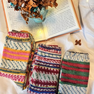 Könnte beinhalten: Drei Paar handgestrickte Wollsocken mit farbenfrohen Mustern. Ein Paar hat gelbe, rosa und graue Streifen mit geometrischen Motiven. Ein weiteres Paar zeigt ein rot-blau-weißes Fair-Isle-Muster. Das dritte Paar hat rote, grüne und blaue Streifen.