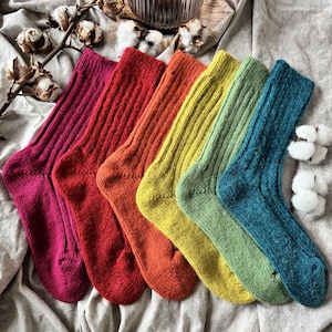 May include: A set of six ribbed knit socks arranged in a spectrum of colours including magenta, red, orange, yellow, light green, and teal. Each sock features a vertical ribbed texture throughout the leg and a smooth knit construction on the foot.