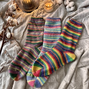 Può includere: Tre paia di calzini lavorati a maglia a mano con vivaci righe orizzontali in varie combinazioni di colori, tra cui tonalità arcobaleno, viola, verde e giallo. I calzini presentano un bordo a coste e una costruzione del tallone standard.