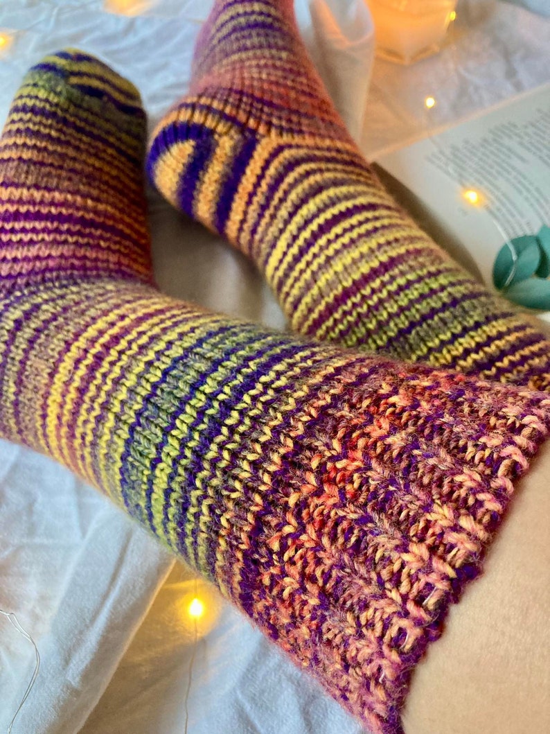 May include: A pair of colorful striped knitted socks in shades of purple, yellow, orange, and pink. The socks are made with a soft, textured yarn and have a comfortable fit.