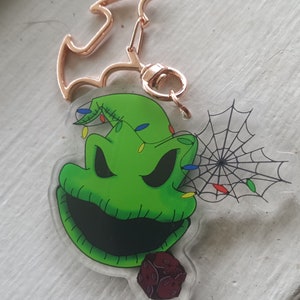 May include: Green and black Oogie Boogie keychain with a red and black dice charm. The keychain features a gold metal bat-shaped key ring.