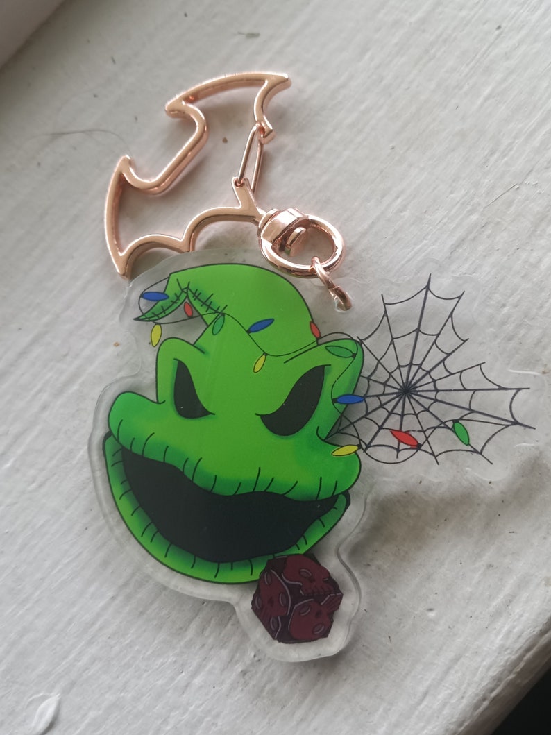 May include: Green and black Oogie Boogie keychain with a red and black dice charm. The keychain features a gold metal bat-shaped key ring.