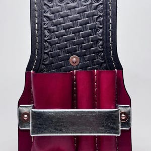 May include: A burgundy leather tool holder with a metal handle and three pockets. The holder has a black leather flap with a woven pattern.