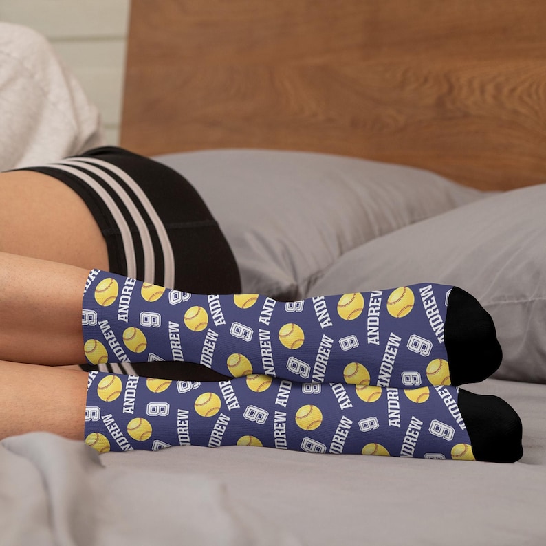 May include: A pair of navy blue socks with a repeating pattern of yellow tennis balls, the name "ANDREW", and the number "8". The socks have black heels and toes.