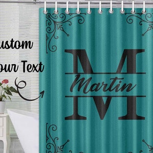 May include: Teal shower curtain with a black monogram design. The monogram is the letter "M" with the name "Martin" written below it. The design is framed with black floral accents.
