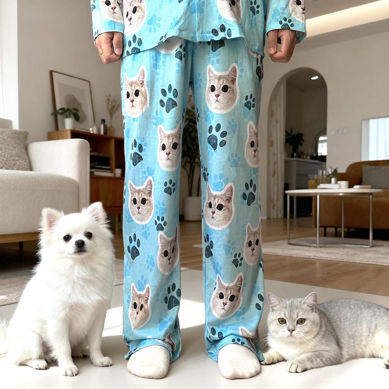 May include: Light blue pajama set featuring cat faces and paw prints. The pajama set includes a long-sleeved top and pants. A white dog and a gray cat are in the foreground.