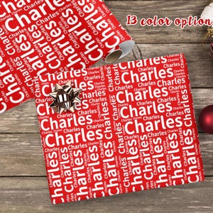 May include: Red and white wrapping paper with the name "Charles" repeated in a white word pattern. The paper is rolled up and there is a silver bow on top of the roll.