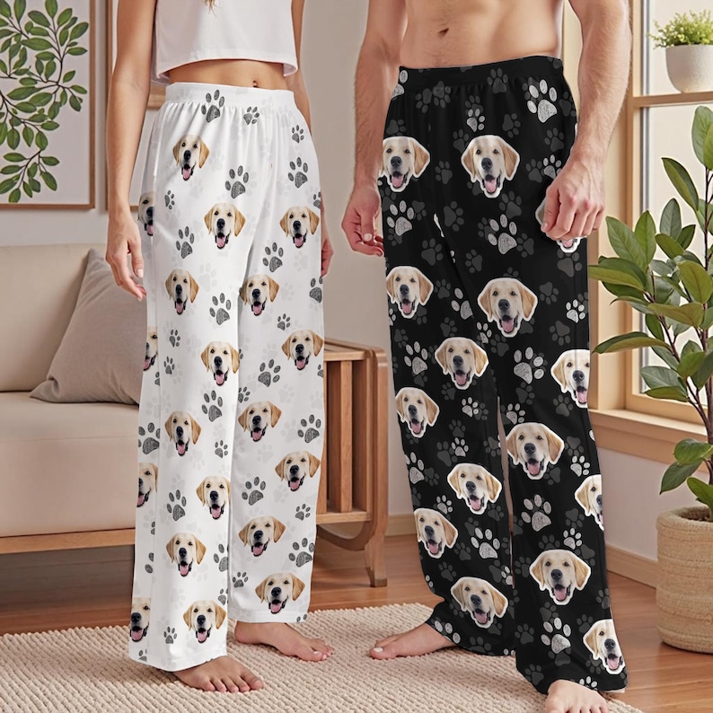 May include: White pajama pants with a repeating pattern of golden retriever faces and gray paw prints. Black pajama pants with the same golden retriever and paw print pattern are also shown.