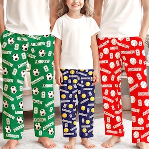 May include: Three pairs of personalized pajama pants in green, navy blue, and red. The green pants feature soccer balls, the navy pants have baseballs, and the red pants have baseballs. Each pair has the name "Andrew" and the number "9".