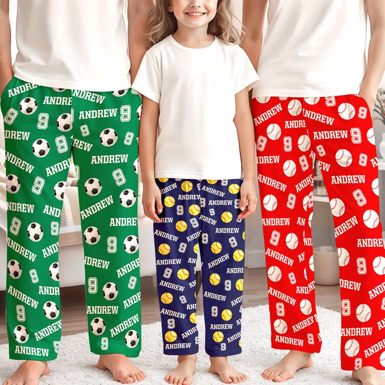 May include: Three pairs of personalized pajama pants in green, navy blue, and red. The green pants feature soccer balls, the navy pants have baseballs, and the red pants have baseballs. Each pair has the name "Andrew" and the number "9".