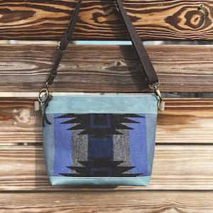 Puede incluir: Un bolso de lona azul y negro con una correa de cuero marrón. El bolso tiene un forro de lona azul claro.