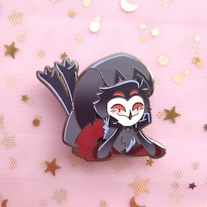 May include: A pin featuring a cartoon owl character in a relaxed pose. The pin has a black and gray color scheme with red accents on the cape and eyes. The owl is smiling, with its head resting on its hands.