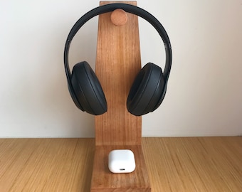 May include: A wooden stand with a black pair of headphones hanging on it. A white wireless charging case is sitting on the stand.