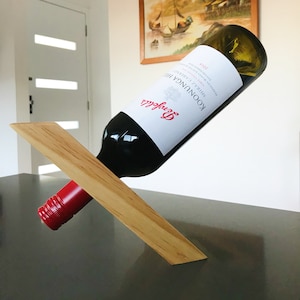 以下が含まれることがあります： 木製のワインボトルホルダーに、赤ワインのボトルが置かれています。ボトルには「KOONUNGA HILL SHIRAZ CABERNET 2018」とラベルが貼られています。