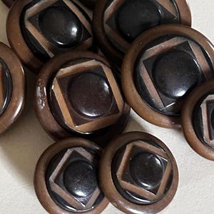 May include: A collection of round buttons featuring a dark brown circular center set within a square frame, surrounded by a smooth, light brown outer ring. Each button has a layered, geometric design with a glossy finish and a raised center.