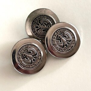 May include: Three circular silver-toned metal buttons featuring a raised eagle emblem in the center. The border of each button is embossed with the text SPES NOSTRA DEVS, surrounded by a beaded edge design on a smooth, reflective metallic surface.