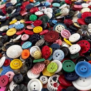 May include: A large assortment of colorful buttons in various sizes and shapes. The buttons are in shades of red, blue, green, yellow, black, white, and pink. Some buttons have multiple holes, while others have decorative designs.