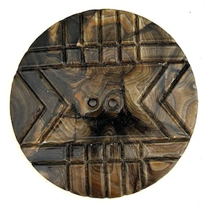 May include: A round, carved wooden button with a geometric design. The button features a dark brown and tan color scheme with two holes in the center. The design includes rectangular and chevron shapes.