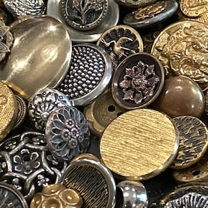 May include: A collection of assorted metal buttons in various shapes, sizes, and finishes. The assortment includes gold, silver, and bronze tones featuring intricate embossed floral, geometric, and bird motifs alongside smooth and textured surfaces.