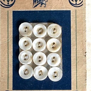 May include: Vintage card of twelve round, off-white mother-of-pearl buttons. The buttons are arranged on a blue background, with the word "Clipper" printed at the bottom. The card has a brown border with decorative elements and the word "Wisconsin".