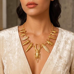 May include: A gold-toned statement necklace featuring a series of metallic beetle and insect charms suspended from a chain. Several of the insect charms are embellished with small, clear crystals, while others have a smooth, polished gold finish.