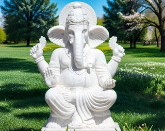 May include: White marble statue of the Hindu deity Ganesha, sitting in a meditative pose with his trunk raised and hands in a mudra gesture. The statue is set against a backdrop of green grass and a blue sky.