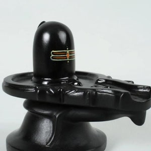 May include: Black Shiva Lingam statue with a three-line symbol on the front. The statue is sitting on a black base with a curved, rounded design.
