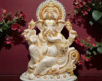 May include: White Ganesha statue with gold accents sitting on a throne. The statue is decorated with jewels and has a large, ornate headdress.